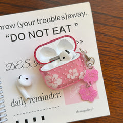 An open clear pink flower AirPods case with a white earbud resting on a white aesthetic daily reminder notebook.