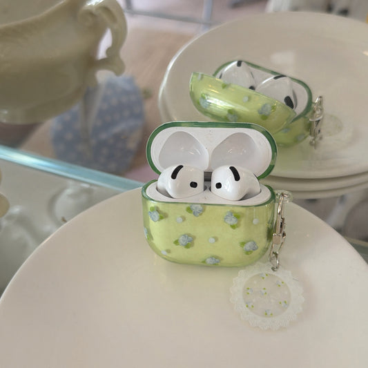 An open translucent green floral AirPods case with wireless earbuds inside, sitting on a white ceramic plate.