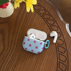 An open light blue polka dot AirPods Pro case with one earbud inside and one resting next to it on a carved wooden table.