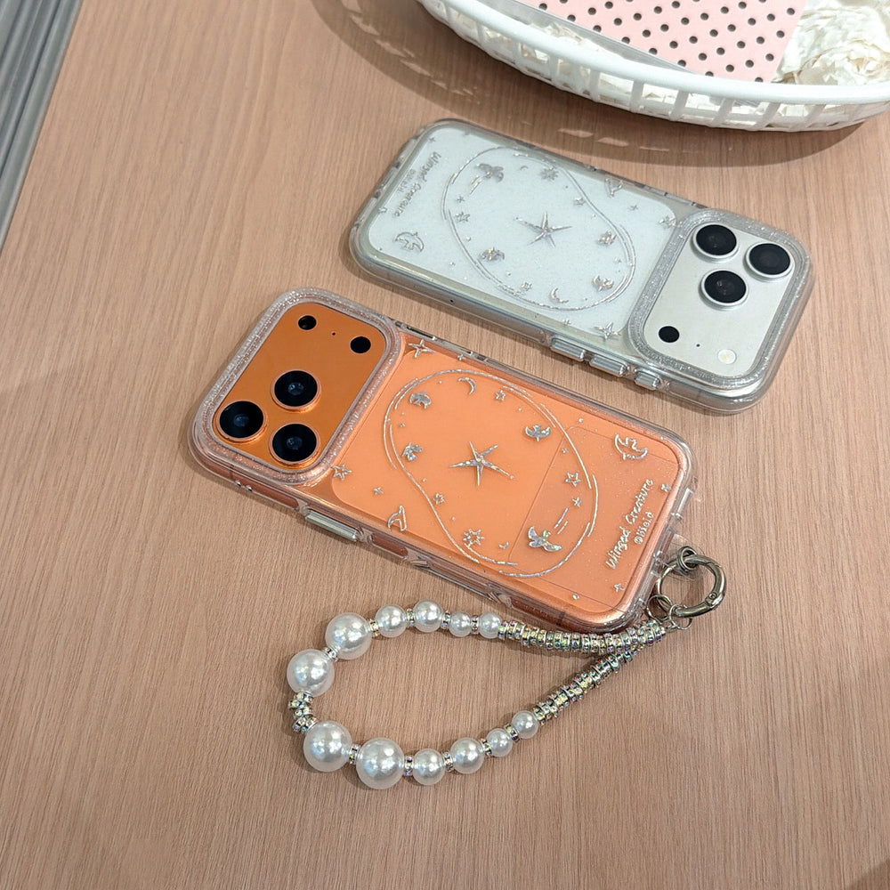 Two glittery iPhone cases in orange and metallic silver displayed flat on a wooden desk, one equipped with a luxury pearl charm strap.