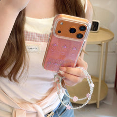 A girl holding an orange iPhone in a clear glitter case with pink roses and a crystal charm lanyard.