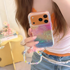Close-up of a rainbow glitter phone cover featuring a bold orange metallic camera lens protection deck and a sparkling crystal bead lanyard.