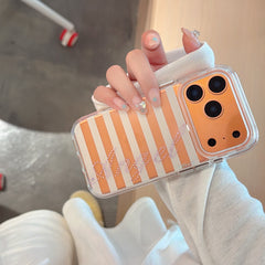 A hand wearing a white sleeve holding an orange and white striped phone case showcasing a pink rhinestone Angel script design.