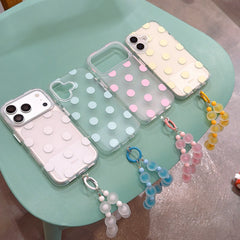 A lineup of white, green, pink, and yellow polka dot iPhone cases with matching beaded charms on a green table.