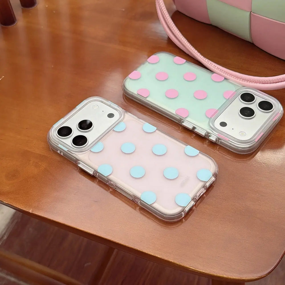 Pastel polka dot clear iPhone cases displayed on a wooden table