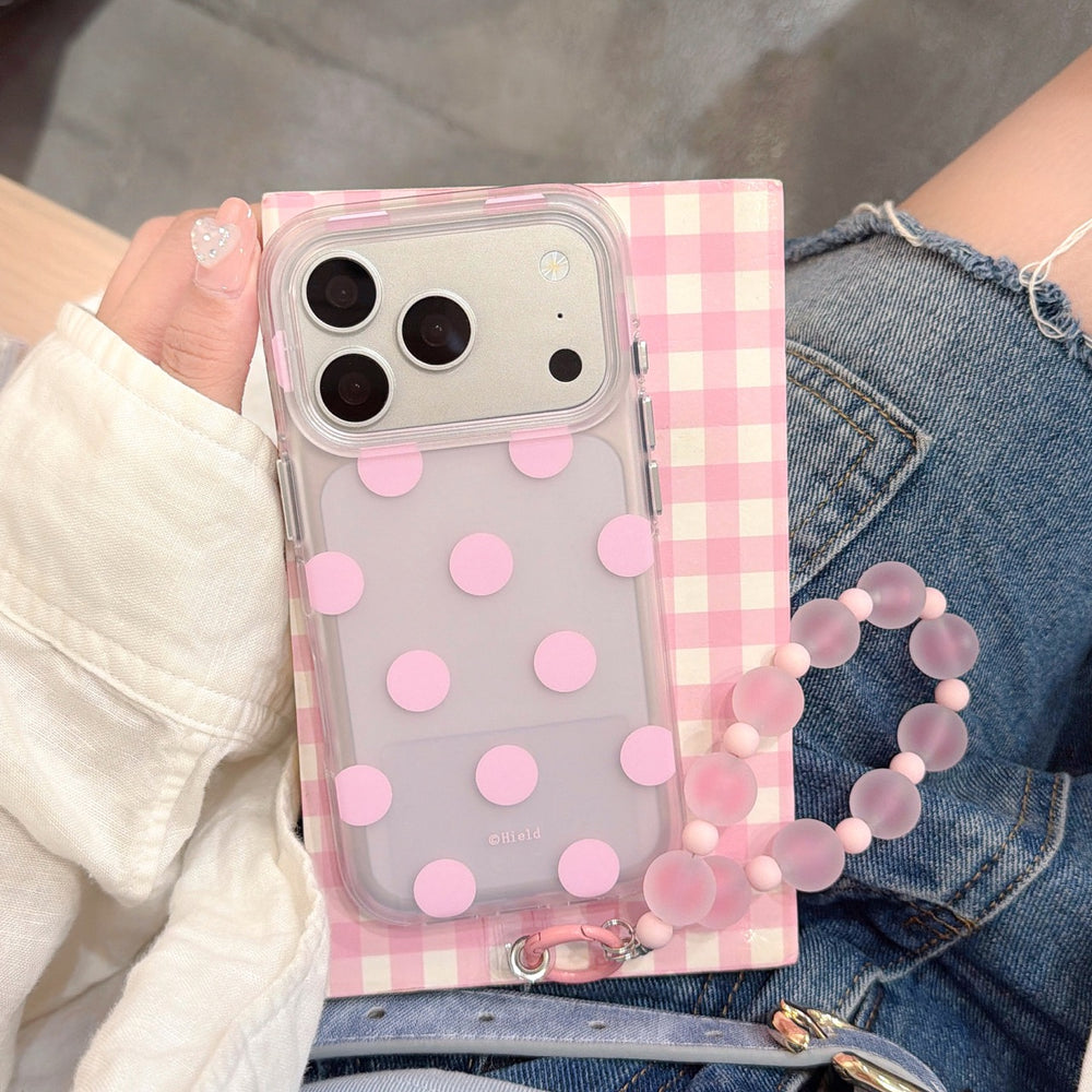 Close-up of a pink macaron polka dot iPhone case held against a pink plaid notebook.