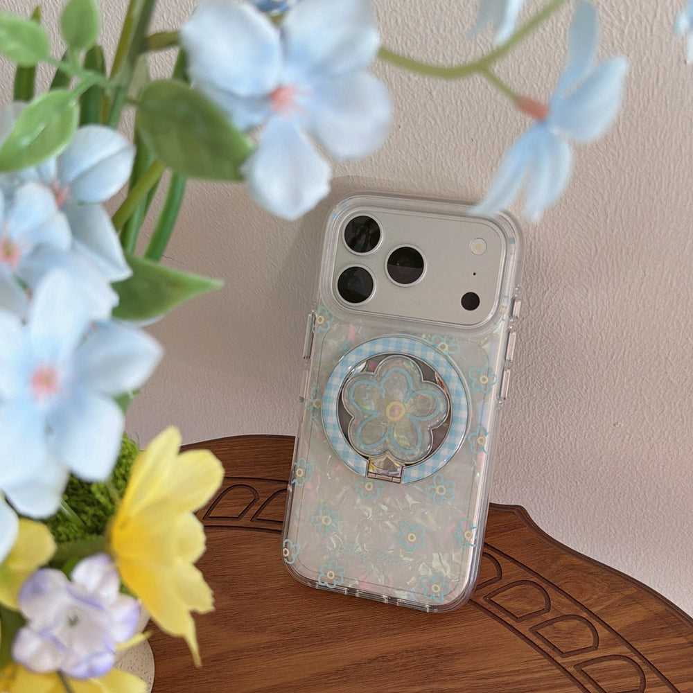 A clear blue flower pearl iPhone case standing on a wooden table behind beautiful blurred light-blue blossoms.
