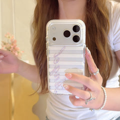 A close-up mirror selfie focusing on a silver and white striped phone cover adorned with a glittery purple rhinestone Angel script.