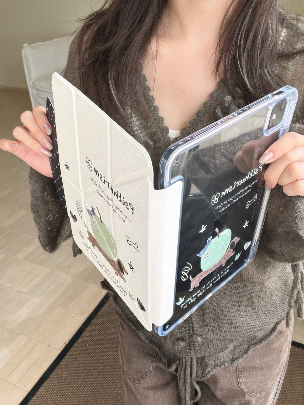 A woman holding a soft girl aesthetic tablet shell open at a V-angle, showing the connection between the clear protective back panel and the cream-colored folding front cover.