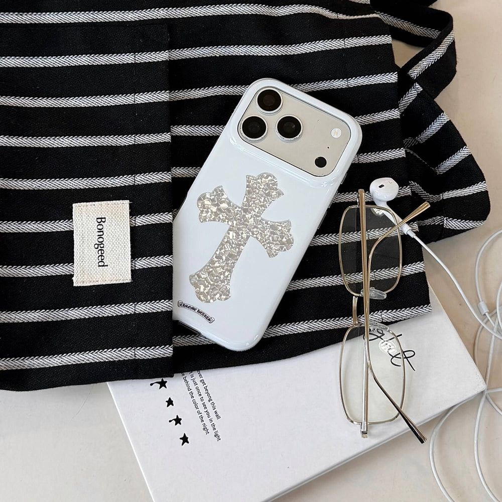 A streetwear Chrome Hearts style silver cross phone case peeking out of a black and white striped tote bag.
