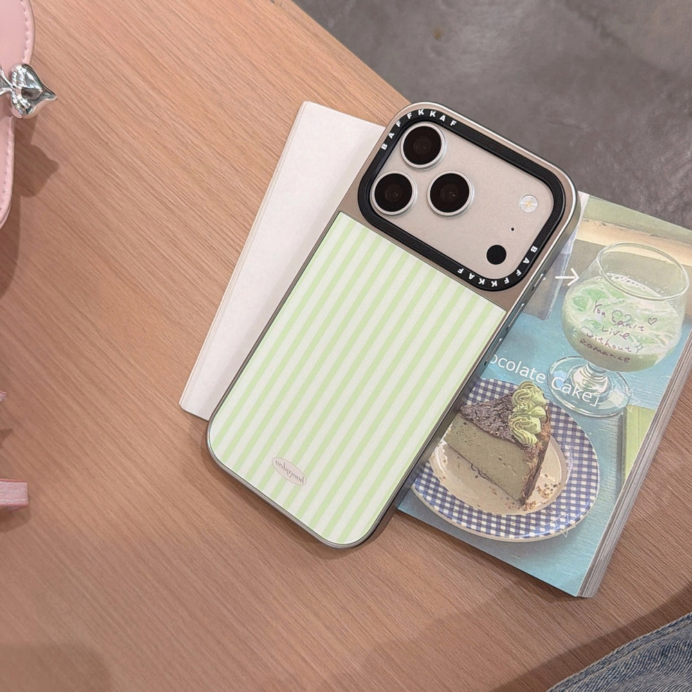 A silver-framed striped iPhone case lying flat on an open aesthetic book on a wooden surface.