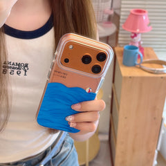 Close-up of a bronze iPhone protected by a clear graphic case featuring blue oil-painted sea waves and a tiny beach ball.