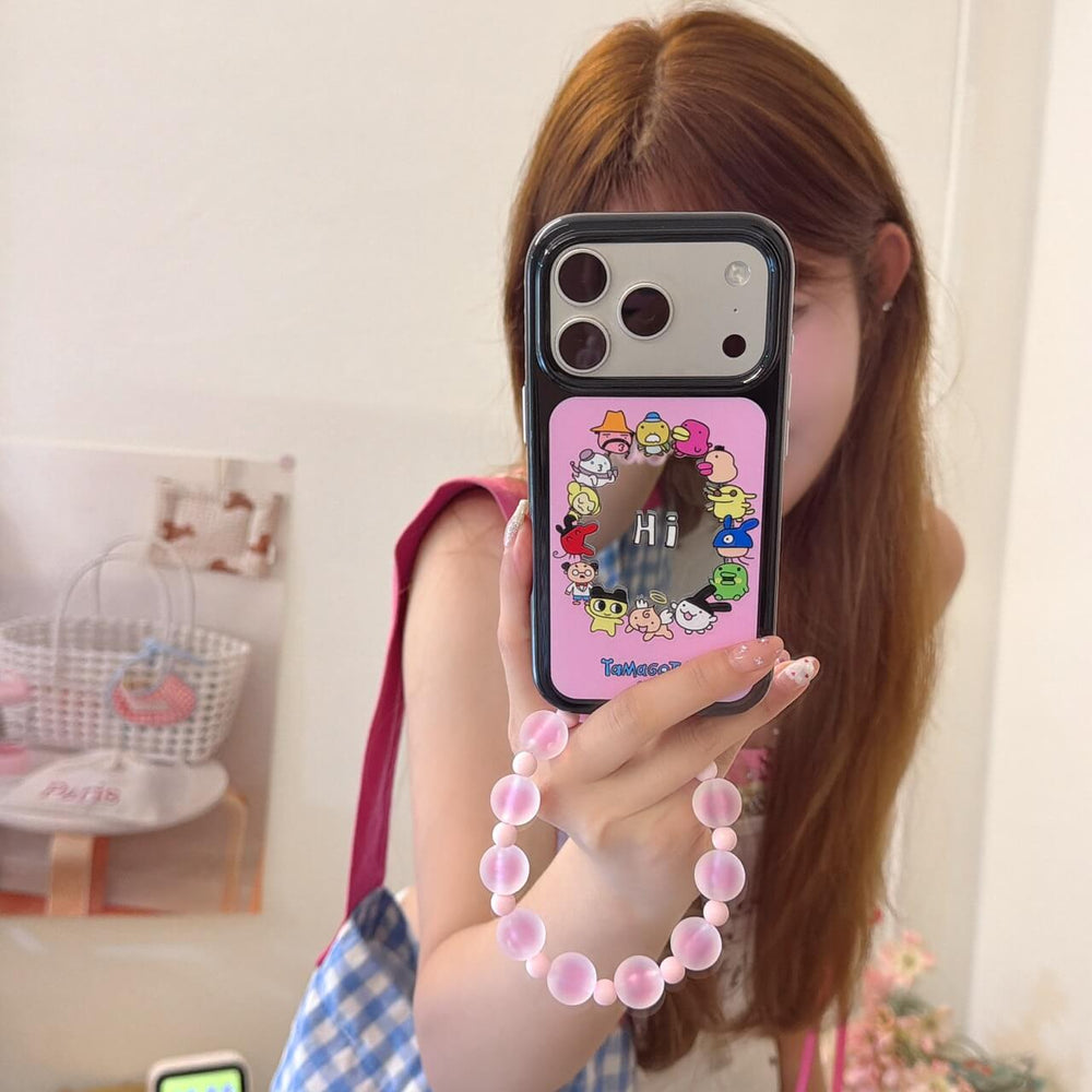 A mirror selfie showing a pink Tamagotchi mirror iPhone case with a silver camera plate and pink beaded strap.