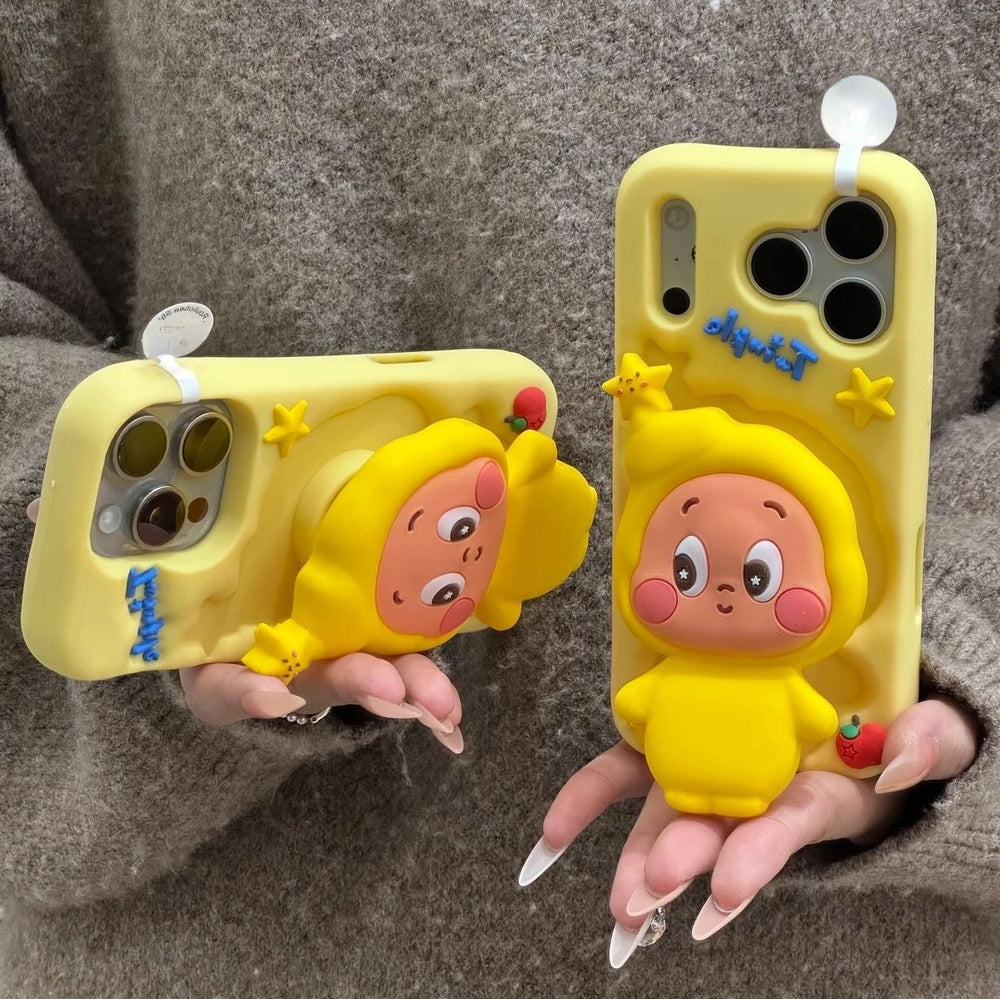 Close-up lifestyle shot of a person holding two yellow silicone Twinkle Twinkle phone cases against a gray knit sweater, demonstrating both the vertical view and the functional horizontal kickstand feature of the 3D pop-up character.