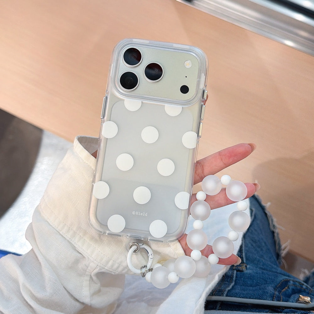A hand holding a white polka dot clear iPhone case featuring a frosted white beaded wrist strap.
