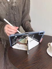 A close-up of a y fold trifold ipad case with pencil holder folded into a triangular stand on a dark wooden cafe table, with a hand holding a white stylus nearby.