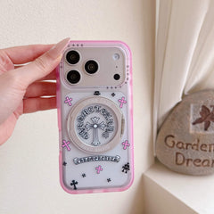 A Y2K Chrome Hearts style pink cross phone case held vertically outdoors next to a rock.