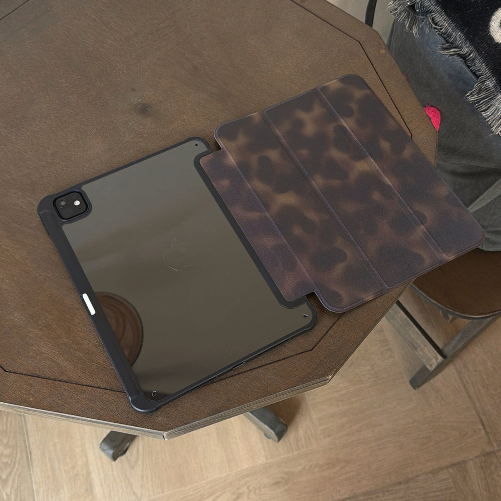 A 2-in-1 magnetic detachable ipad case laid open flat on a wooden table, showing the dark tortoiseshell inner lining pattern next to the clear tinted protective back shell