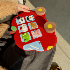 Top-down view of the red apple bus iPad cover resting on a lap, showcasing six 3D cartoon animals in blue windows, a green leaf stem, and two large brown wheels with yellow centers.