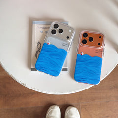 Two summer ocean-themed phone covers for silver and bronze iPhones lying on a white round table next to a notebook.