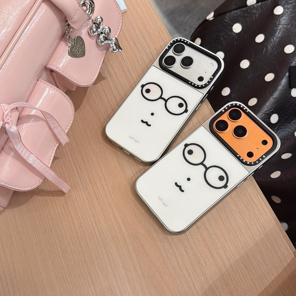 Two aesthetic geek face phone cases in silver and orange camera variants on a wooden table.