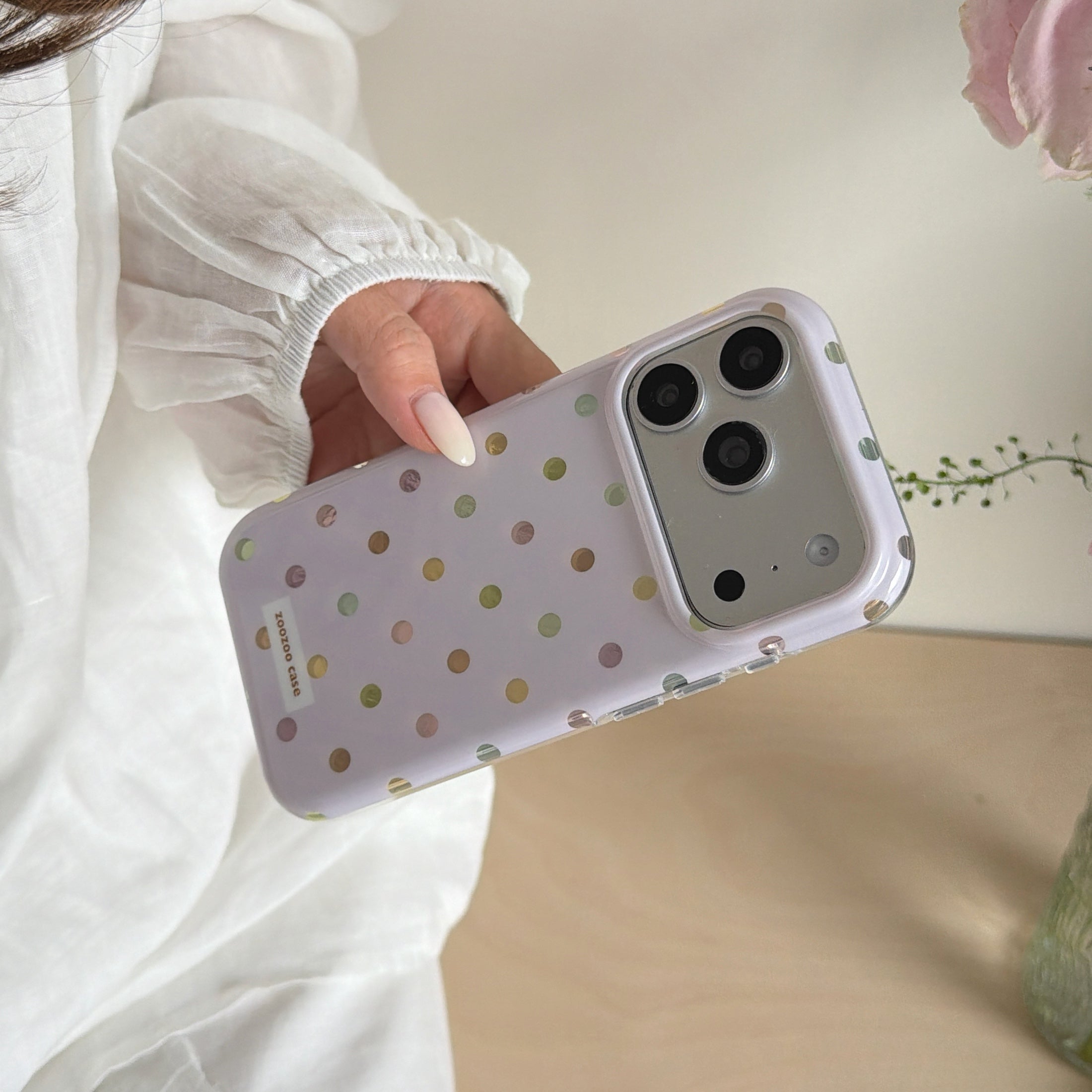 A hand holding a lavender polka dot phone case showcasing its clear protective bumper edge.