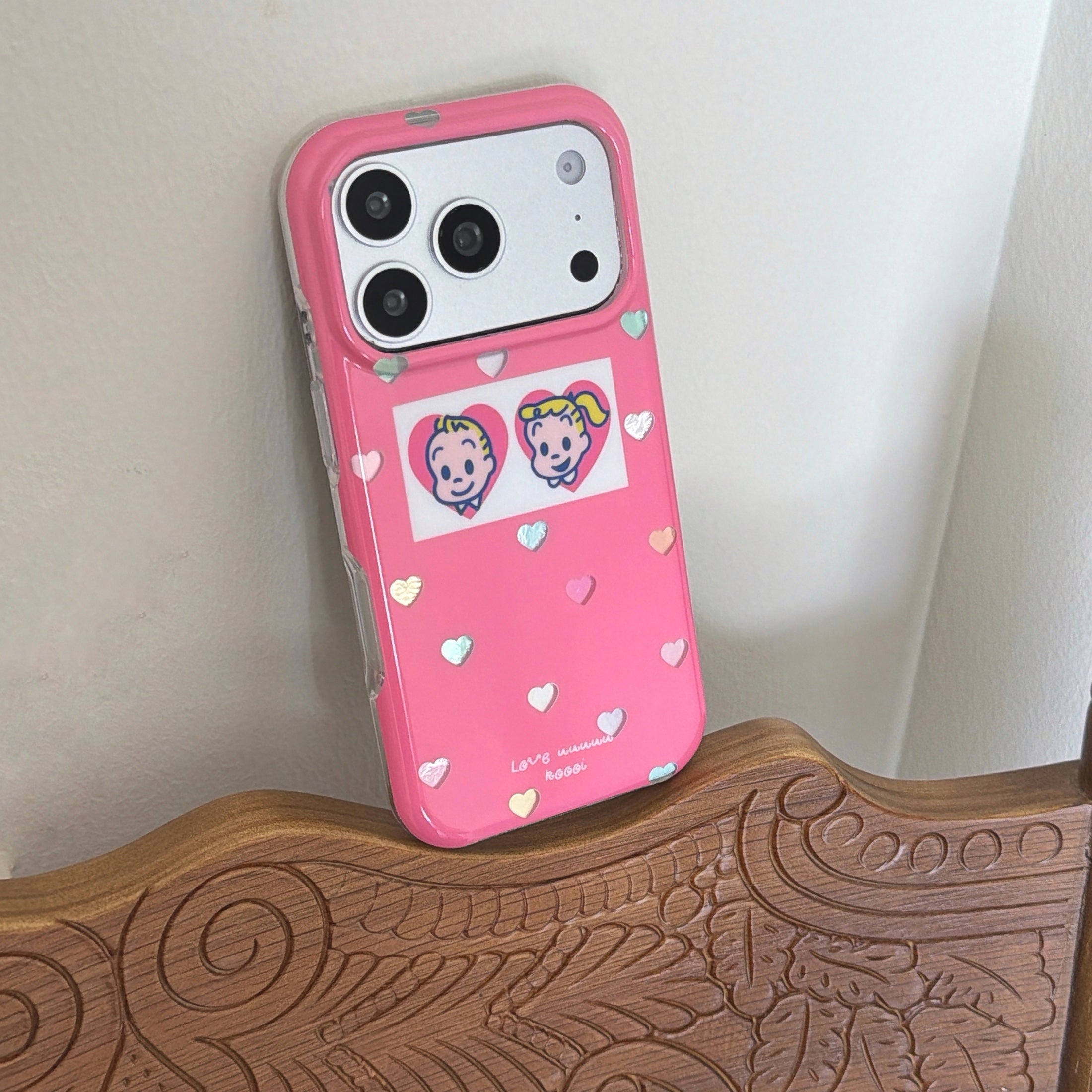 An aesthetic pink Osamu Goods iPhone case propped vertically on an ornate wooden chair.