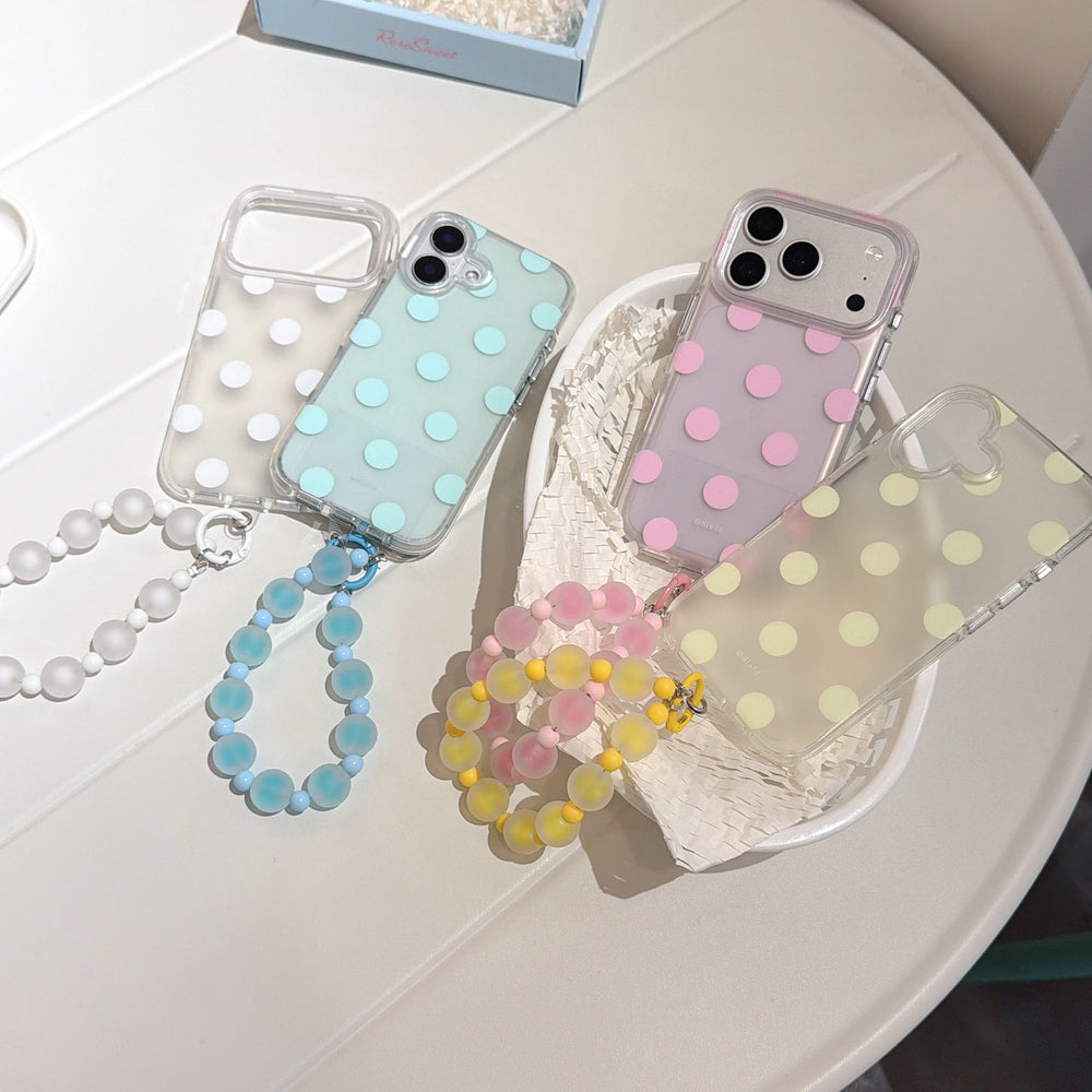 Flatlay of four pastel polka dot iPhone cases with colorful jelly beaded straps in a studio tray.