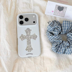 A white aesthetic phone case with a silver cross logo lying on a white sheet with a plaid scrunchie.