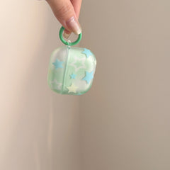 A hand lifting a translucent mint green starry AirPods case by its attached green ring carabiner.