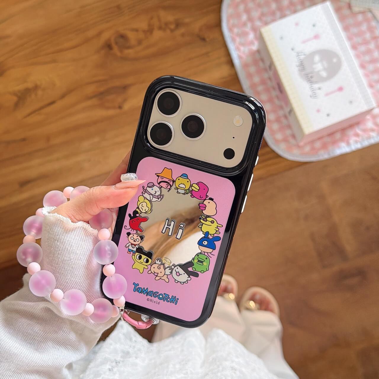 An aesthetic view of the pink Tamagotchi character mirror phone case held next to a pink canvas bag.