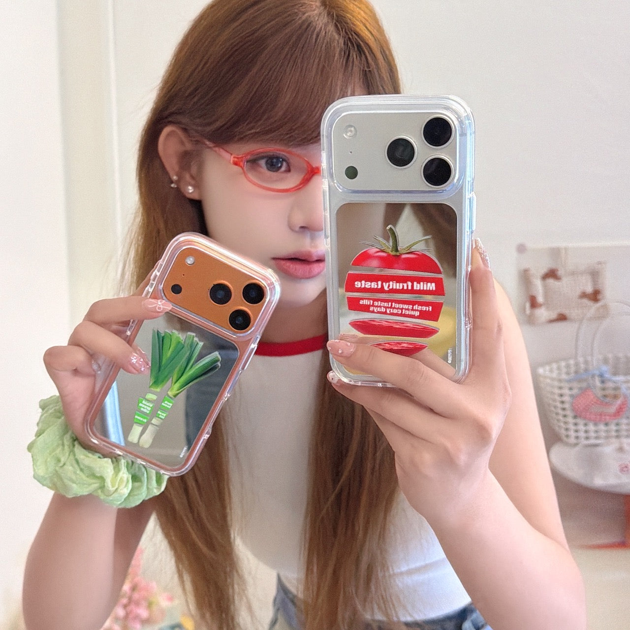 A girl holding two different aesthetic vegetable mirror phone cases featuring clear orange and silver borders.