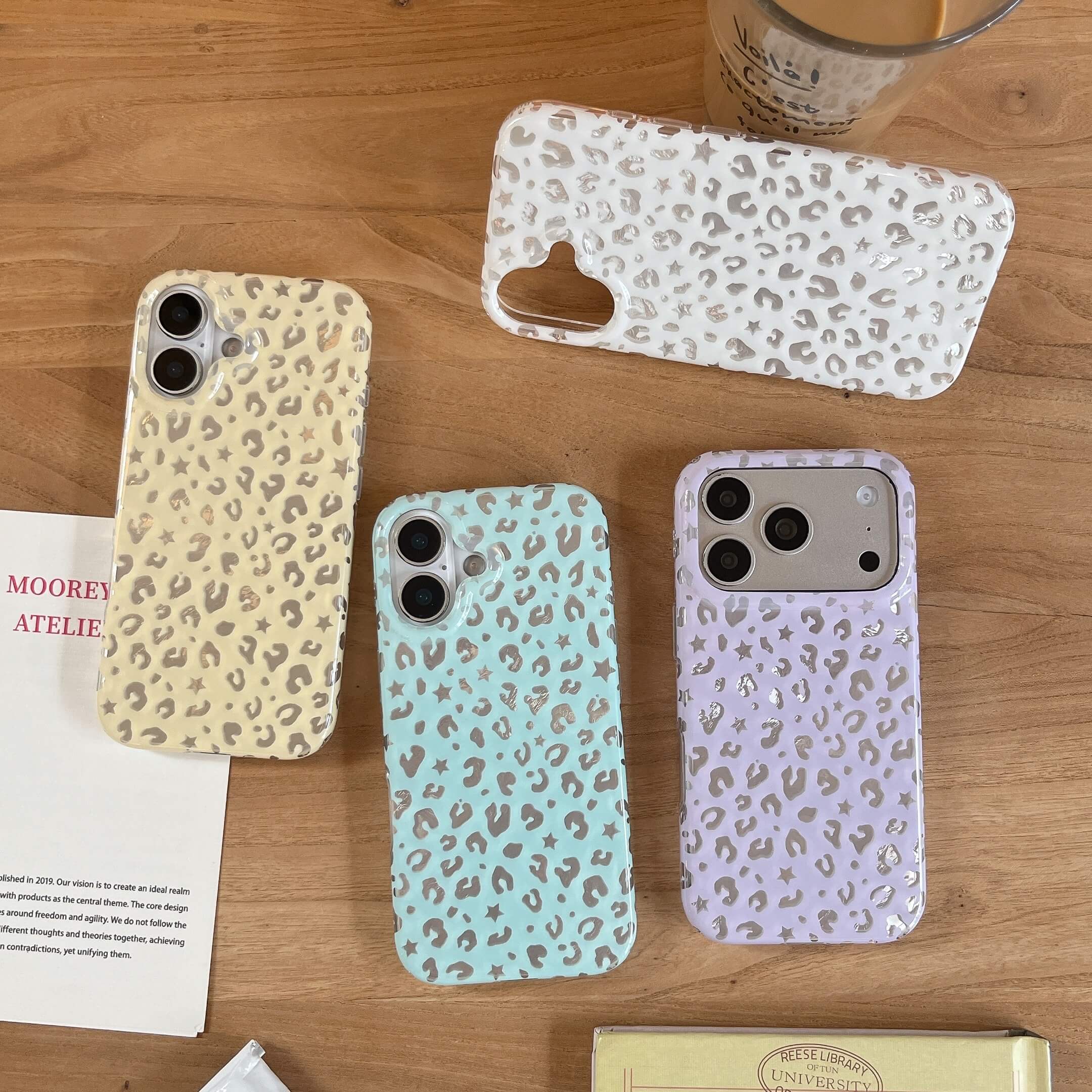 Four colorful aesthetic Y2K star leopard iPhone cases in beige, white, mint green, and lavender on a wooden table.