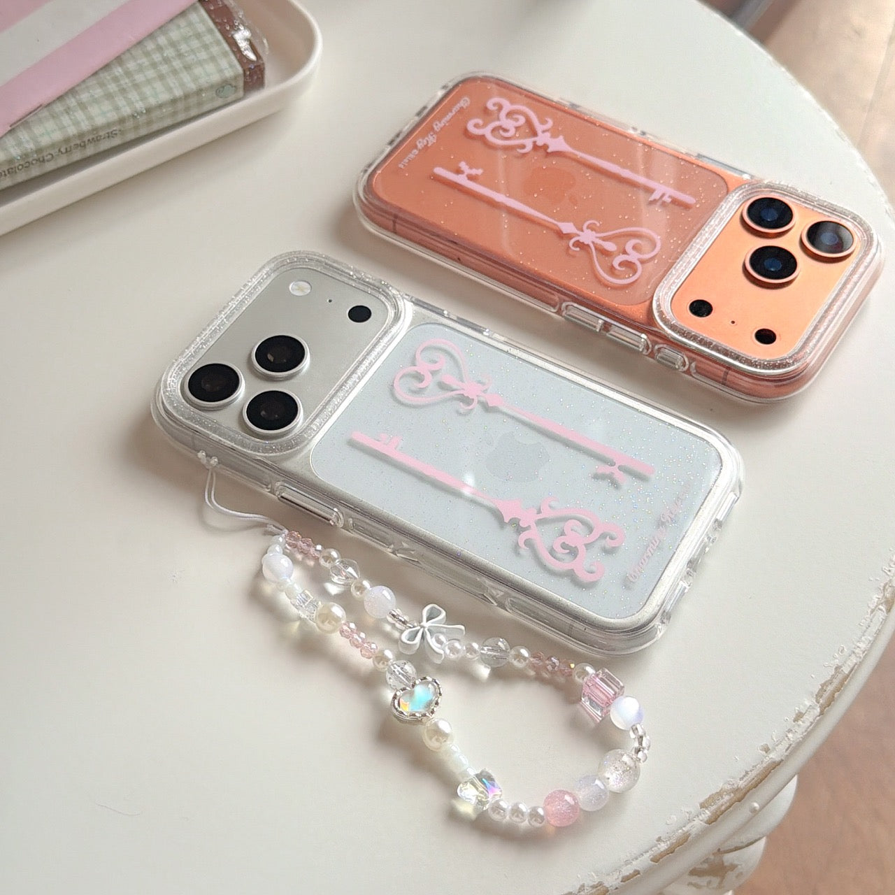 Two balletcore aesthetic charming key phone cases in silver and orange glitter lying flat on a white table.