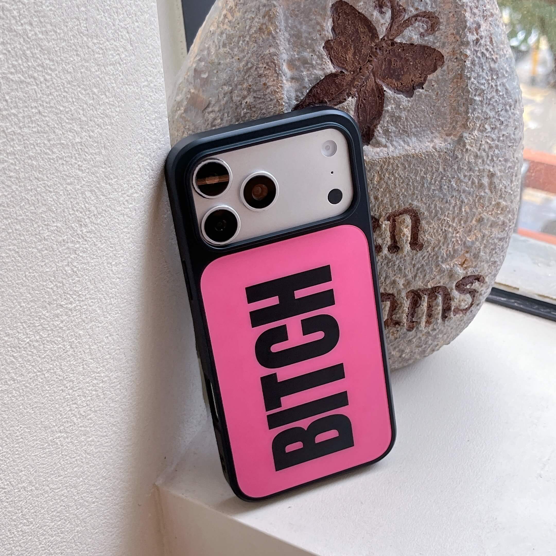An edgy hot pink graphic phone case leaning against a decorative stone outdoors.