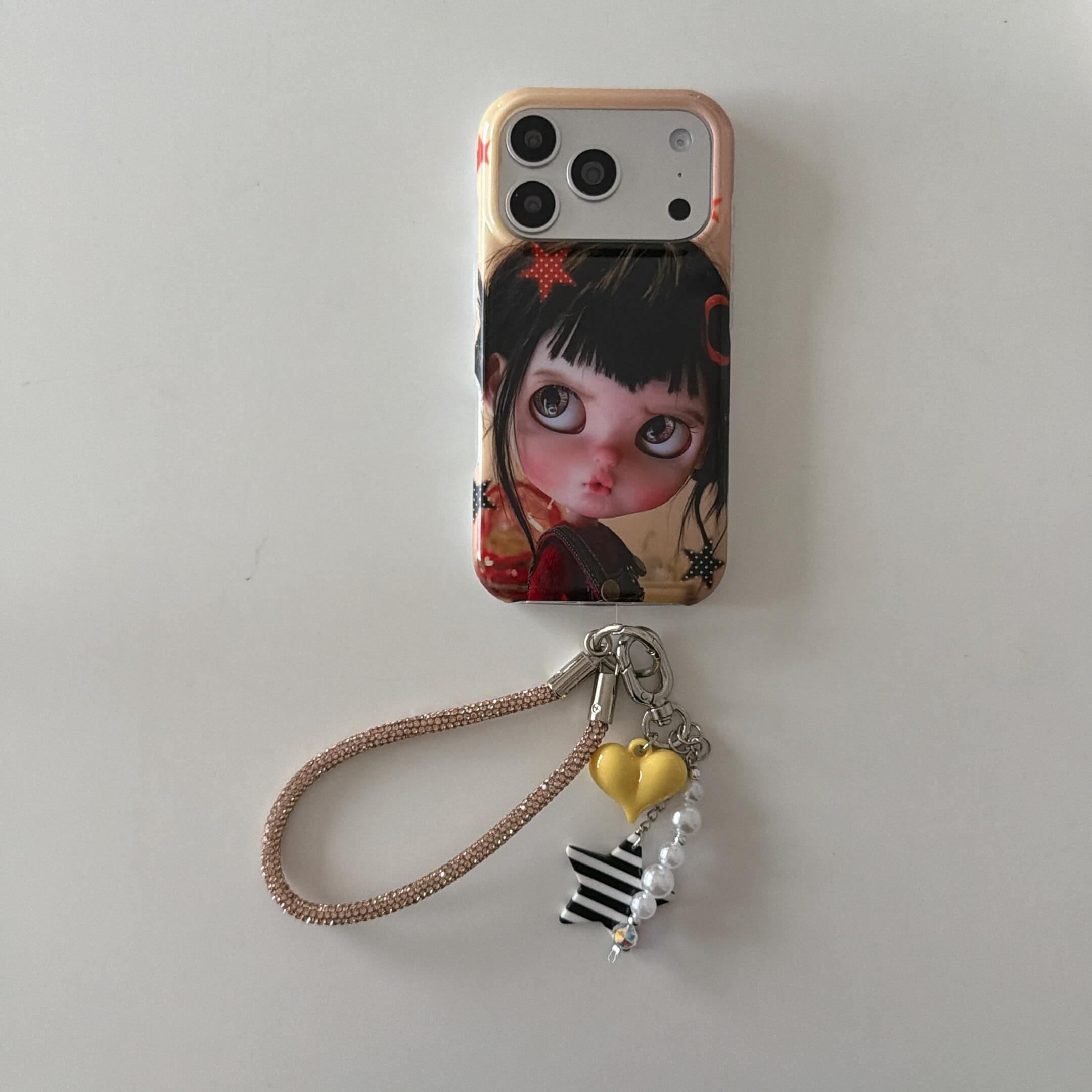 Black-haired big-eye doll iPhone case with heart and star charm wrist strap.
