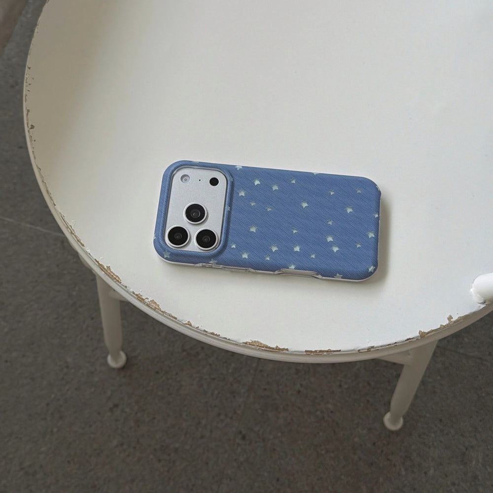 An aesthetic blue celestial star iPhone case lying flat on a white wooden side table.