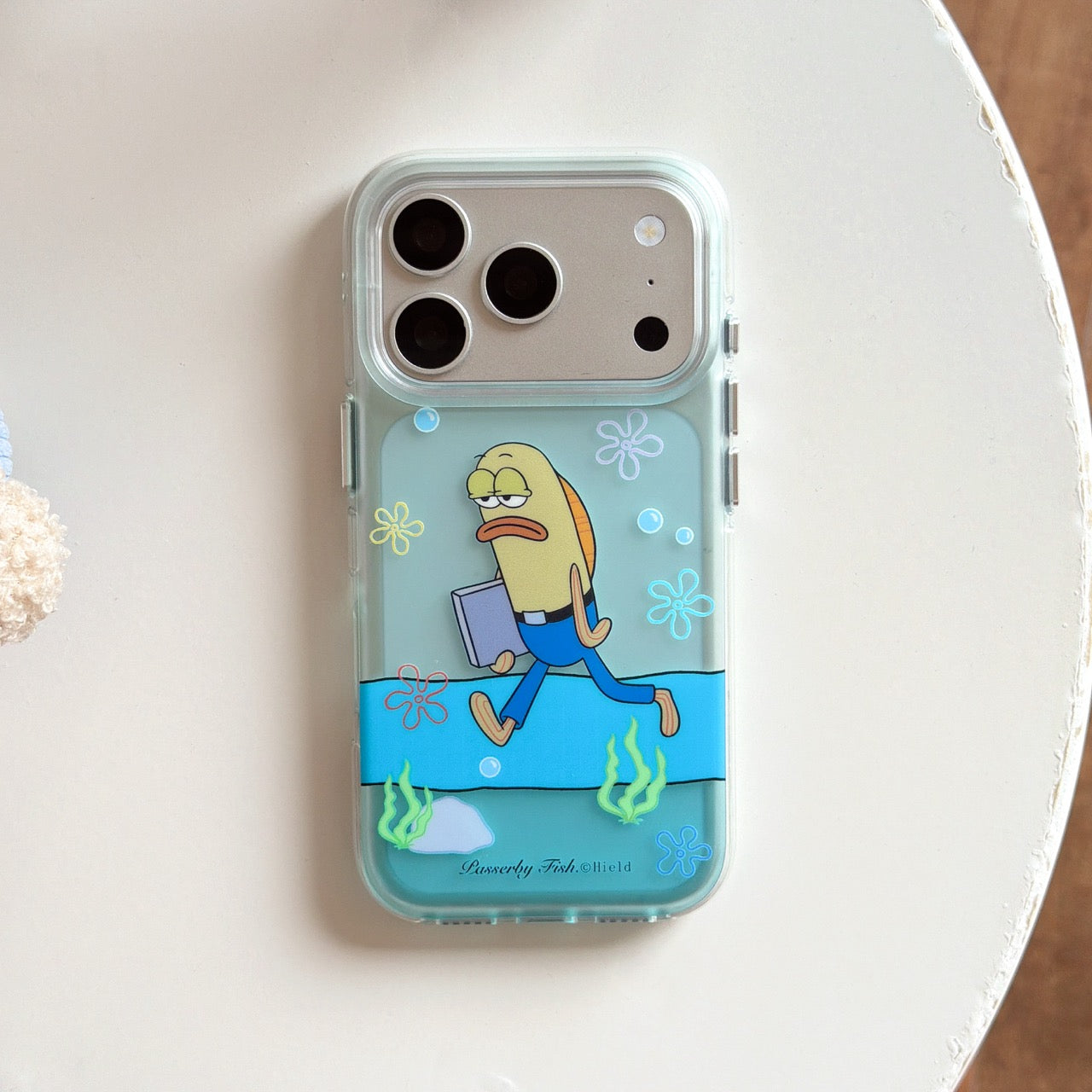 A top-down view of a mint green clear iPhone case featuring a walking business fish graphic on a clean white surface.