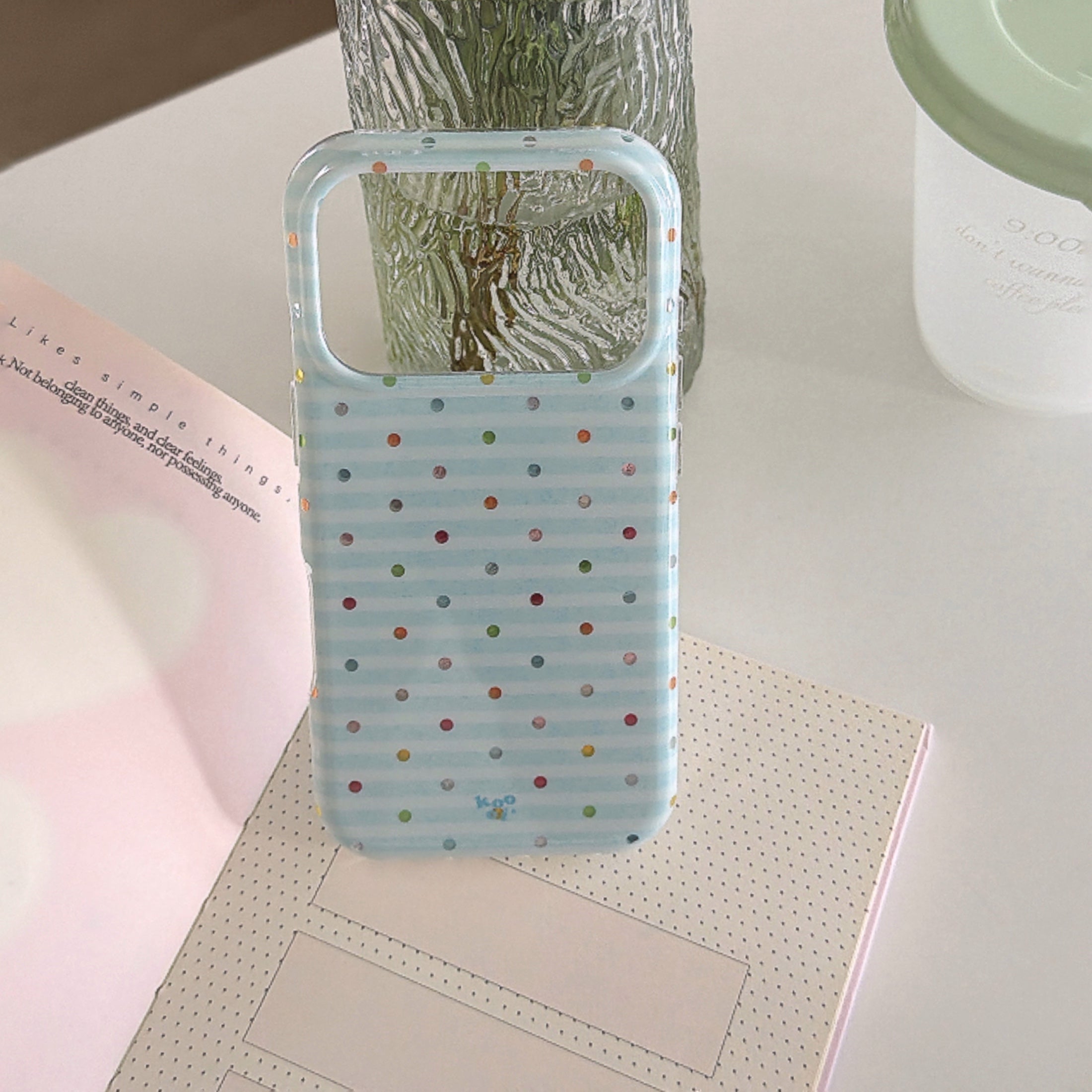 An empty blue stripe phone case shell propped open on a notebook next to a glass vase.