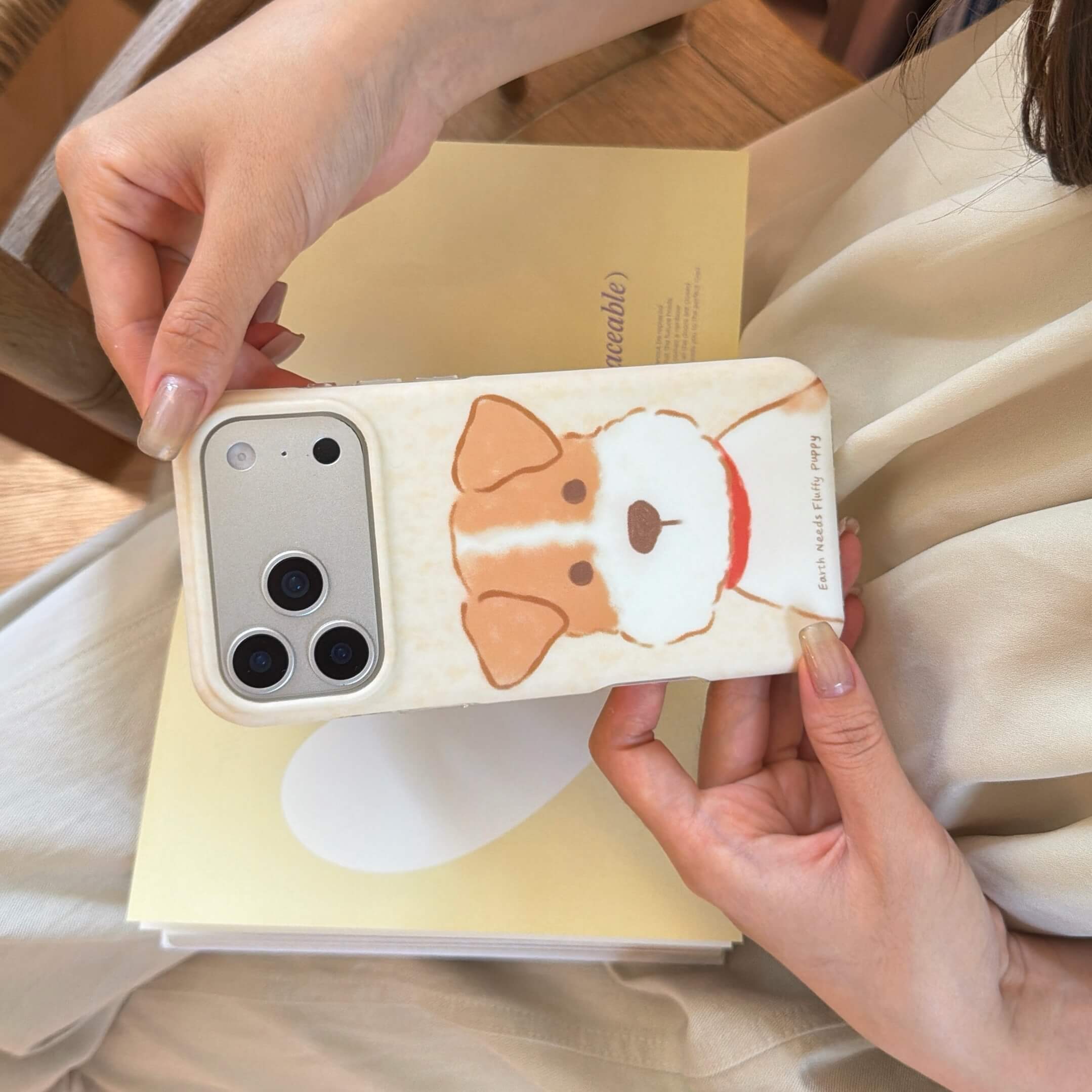 Horizontal view of a cream dog iPhone case with brown and white puppy artwork.