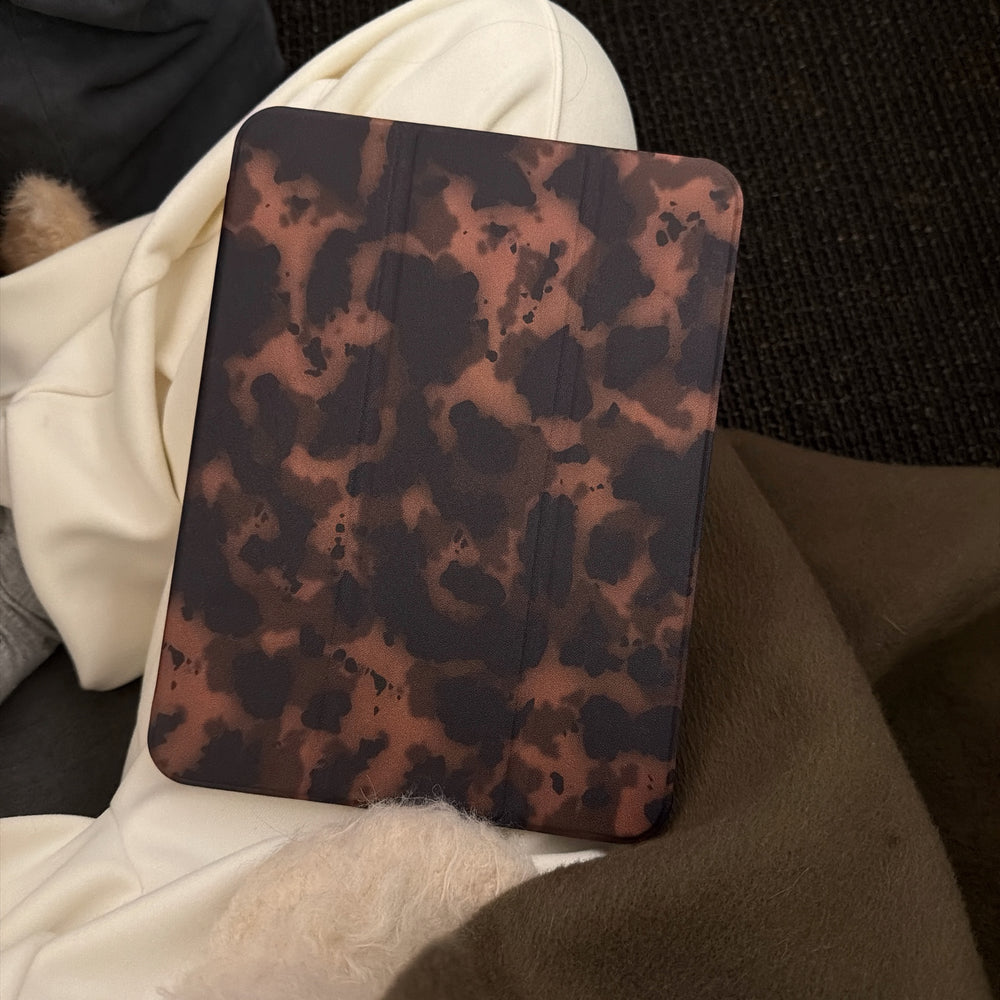 Close-up of a chic tortoiseshell ipad case front cover resting on cozy cream and brown winter clothing, showcasing the luxury dark animal print pattern.