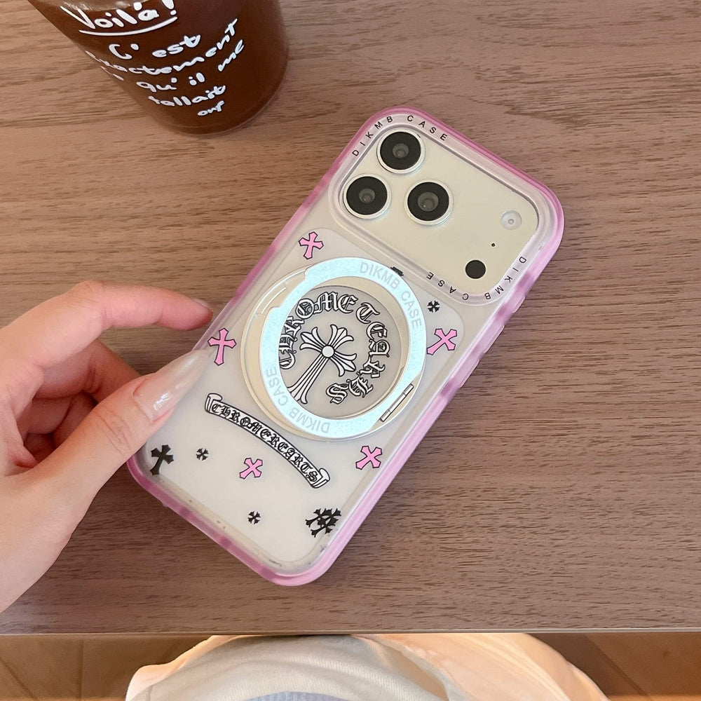 A Chrome Hearts cross pink phone case on a wooden desk next to a cup of iced coffee.