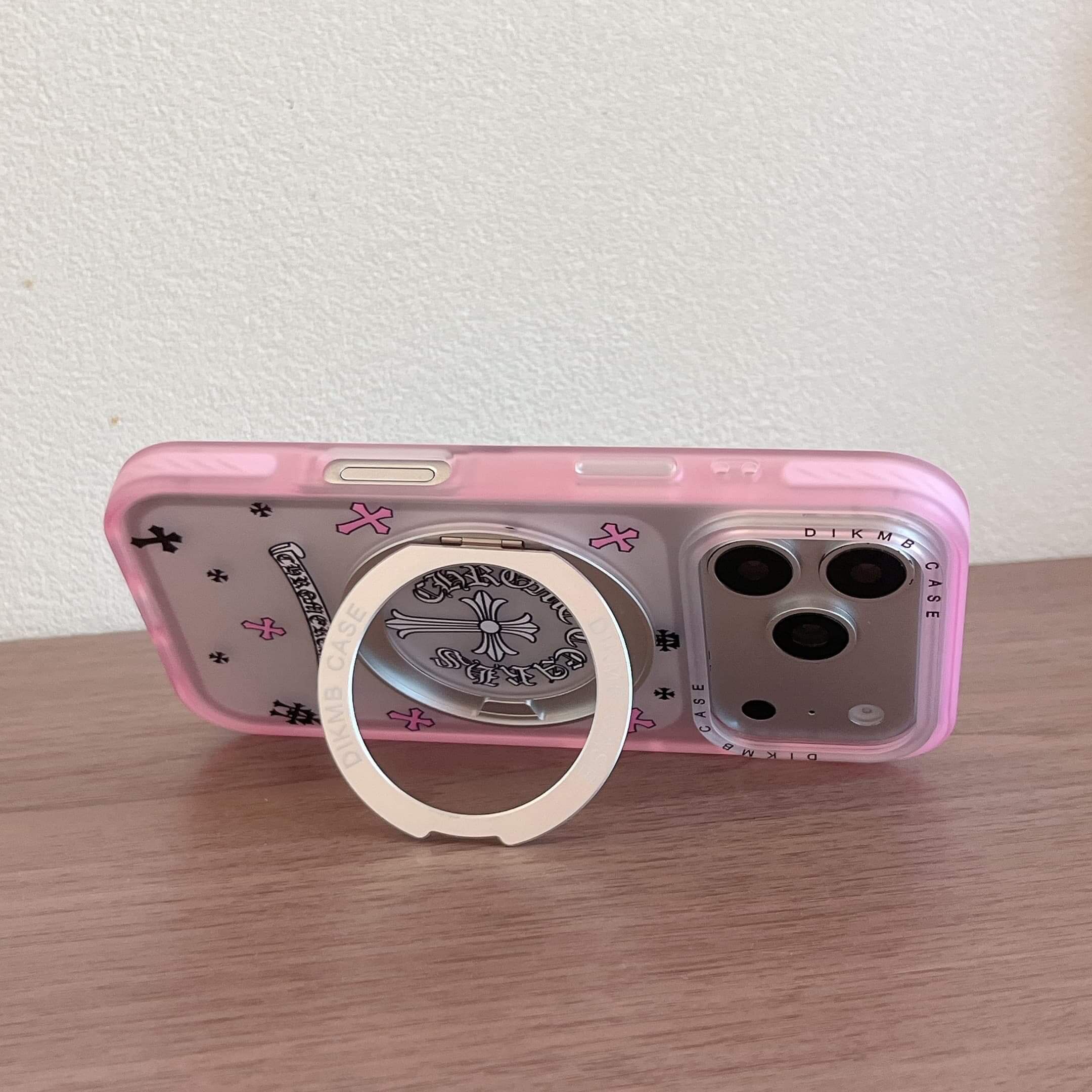 A Chrome Hearts style phone case propped horizontally on a table using its metal ring stand.