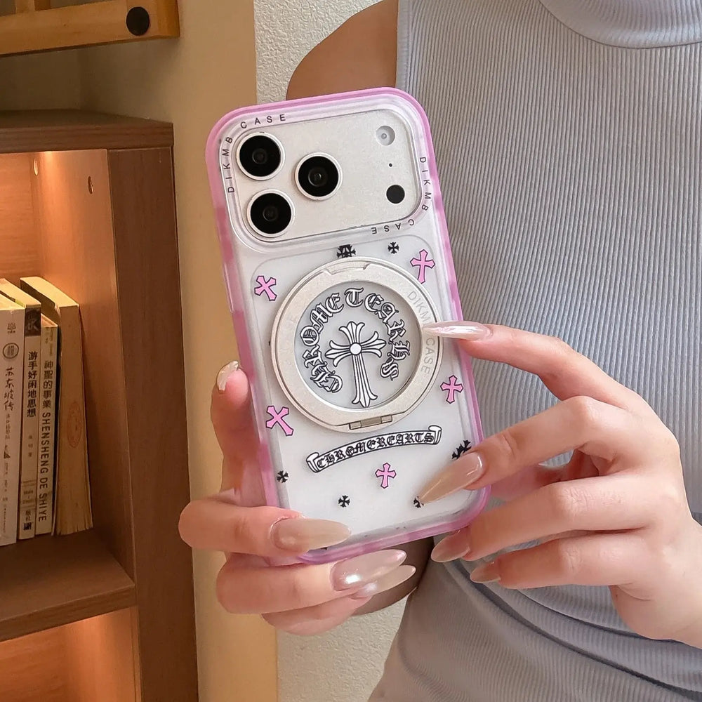 Hand holding a Chrome Hearts style pink cross iPhone case with a silver metal ring holder.