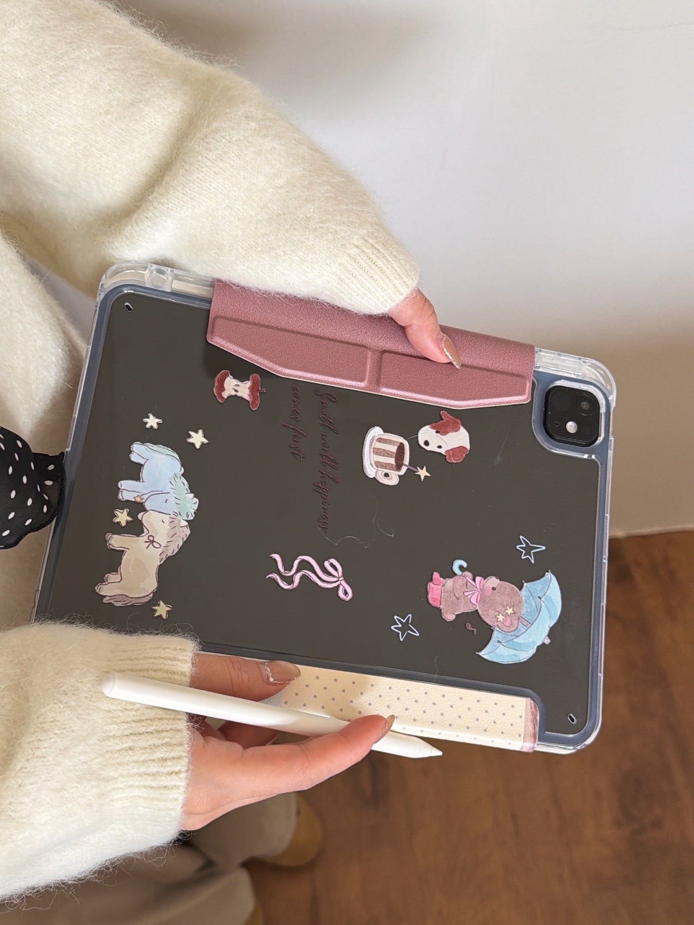 Rear view of an aesthetic clear back iPad case with printed cartoon graphics held horizontally, highlighting the pink magnetic closure clasp.