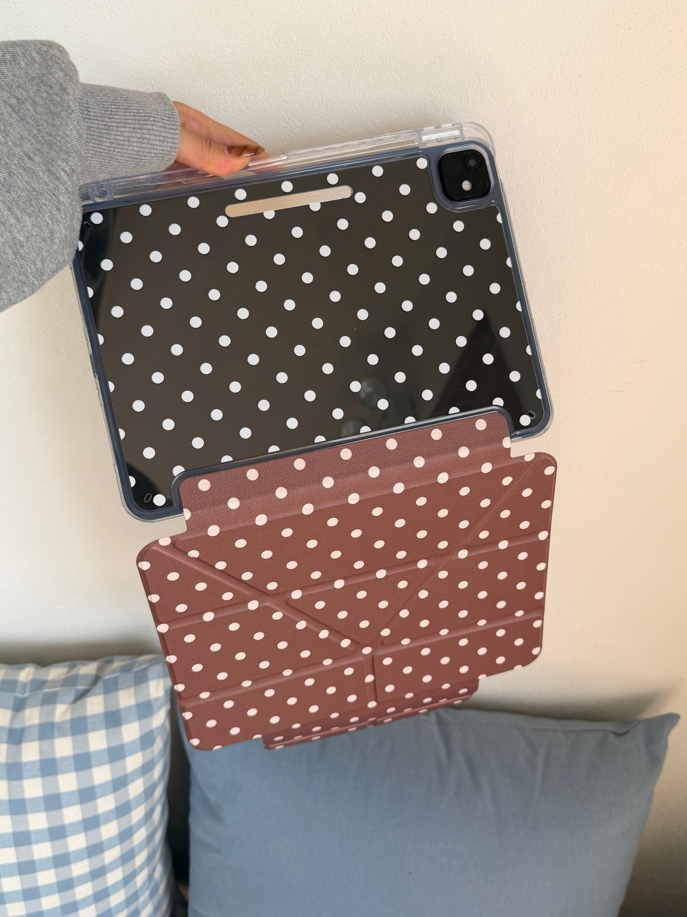 A hand holding up a clear back panel ipad smart cover showing the transparent shell with white dots and the hanging taupe brown geometric front flap.