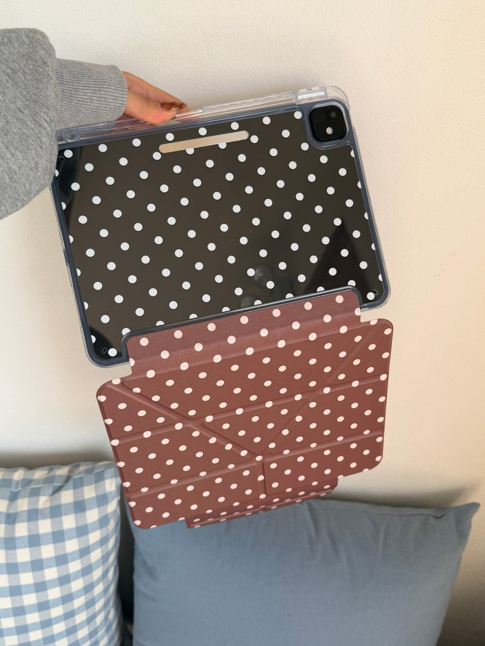 A hand holding up a clear back panel ipad smart cover showing the transparent shell with white dots and the hanging taupe brown geometric front flap.