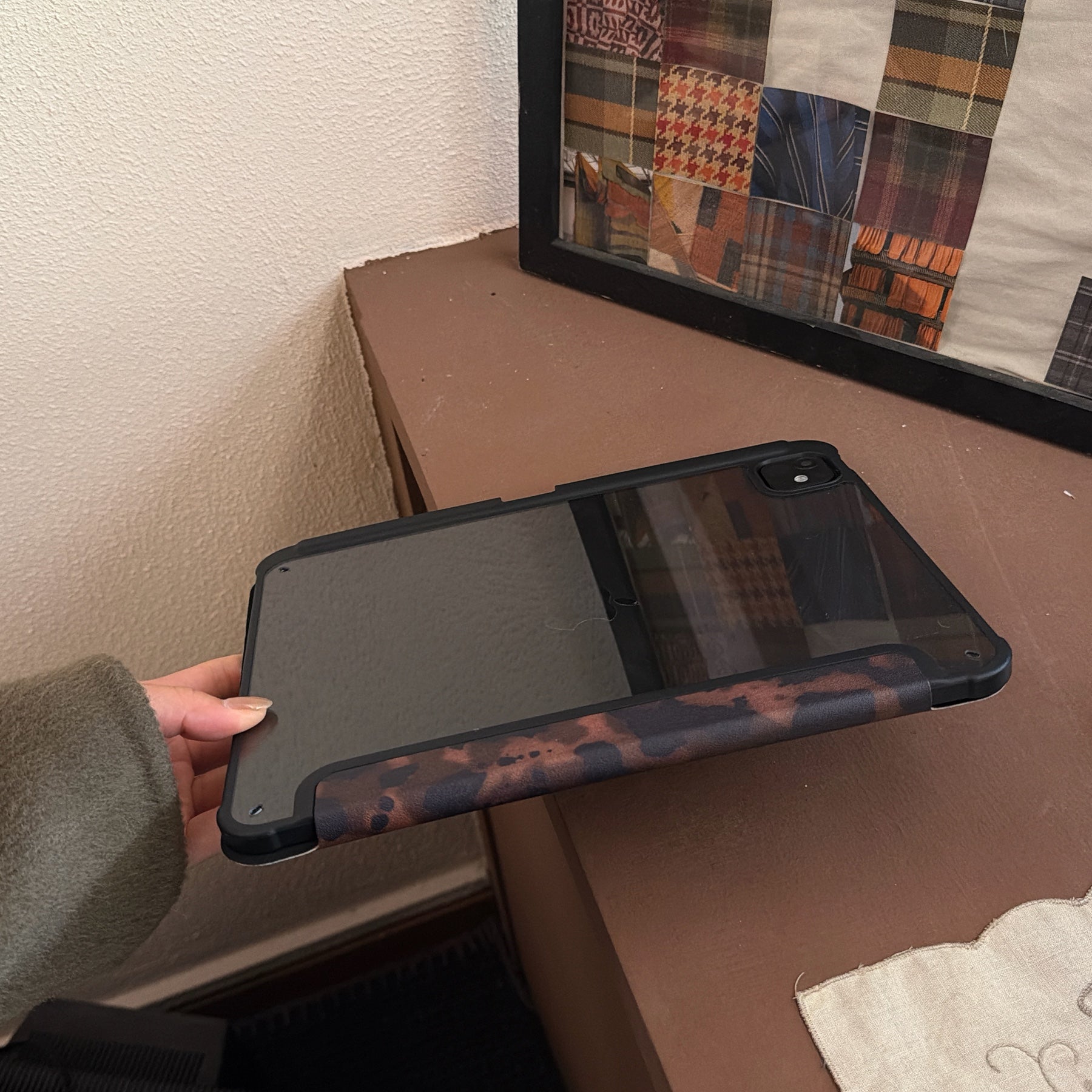 A hand holding up the clear back tablet cover with pencil holder, showing off the premium translucent tinted matte finish and the edge of the dark tortoiseshell magnetic flap.