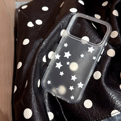 A clear shockproof phone case shell printed with white stars lying on a black and white polka dot leather surface.