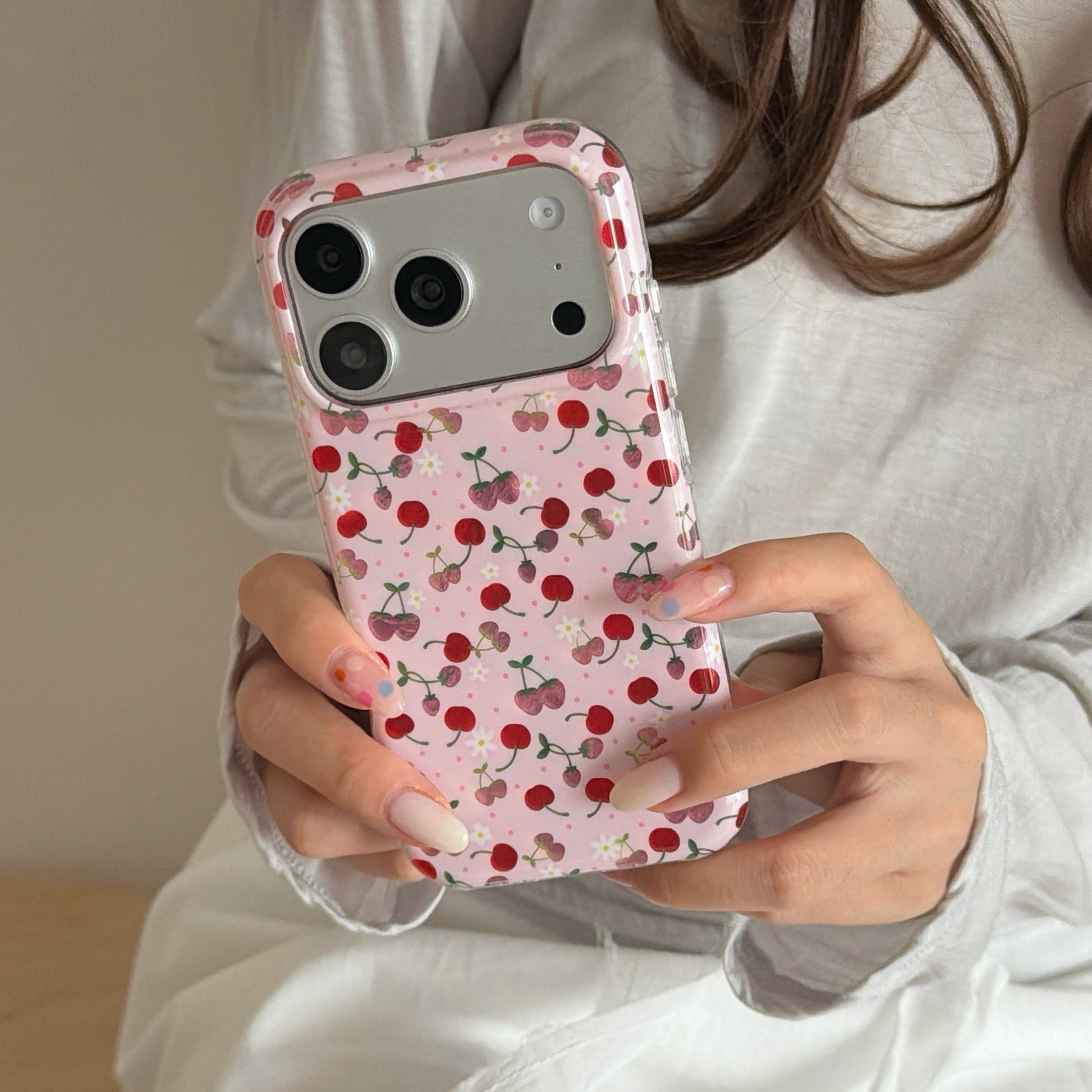A close-up of a girl holding a coquette aesthetic pink cherry phone case with both hands.